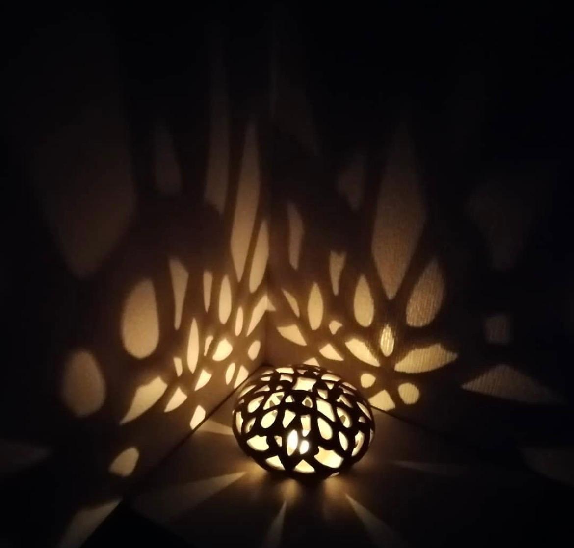 Illuminated spherical openwork ceramic form casting patterned light and shadow