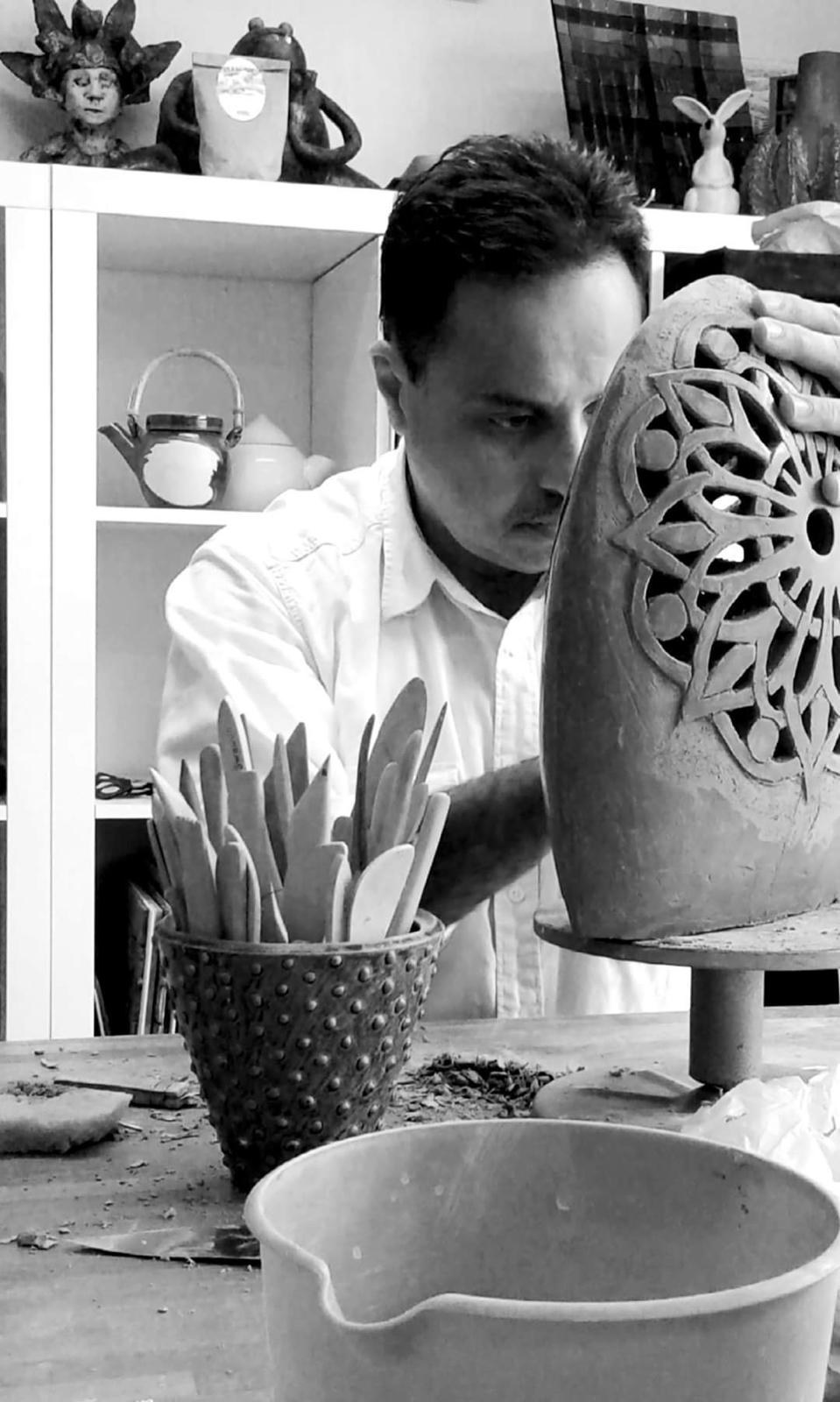 Black-and-white photograph of Raed Askar working on a large pierced ceramic form in his studio